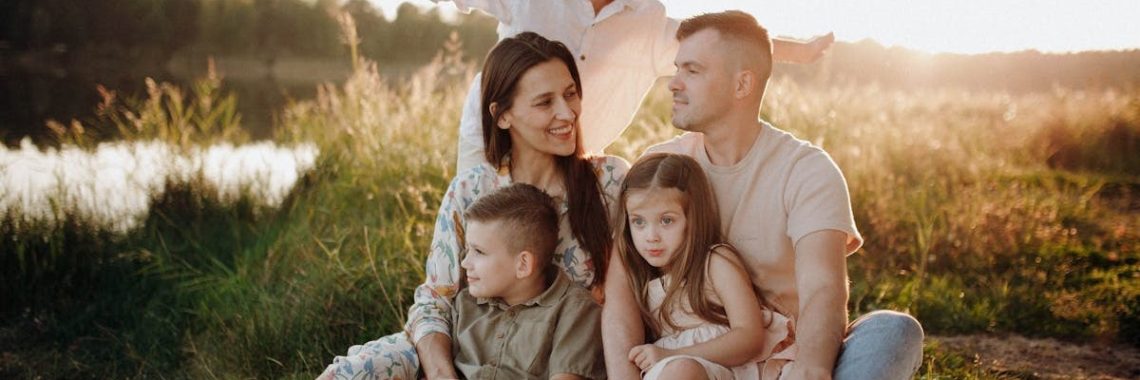 A family of five enjoying a serene picnic in a sunlit meadow during sunset.